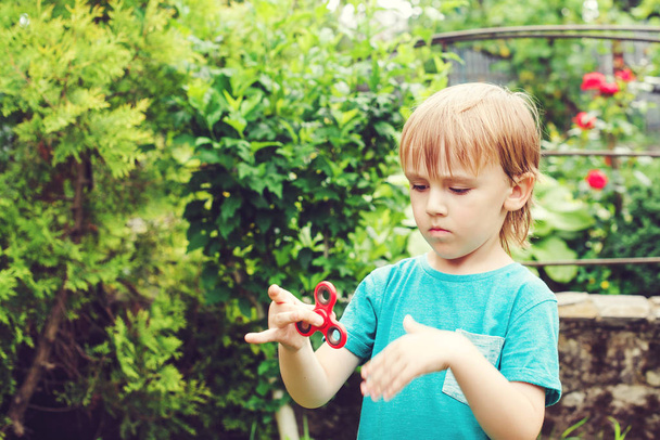 Garçon mignon jouant avec Tri Fidget Hand Spinner à l'extérieur. Jouet tendance pour les mains pour les enfants et les adultes
. - Photo, image