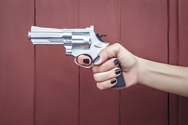 Γυναίκα χέρι με βερνίκι νυχιών, κρατώντας ένα όπλο  - Φωτογραφία, εικόνα