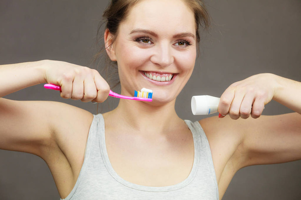 Woman holding toothbrush and placing toothpaste on it - Zdjęcie, obraz