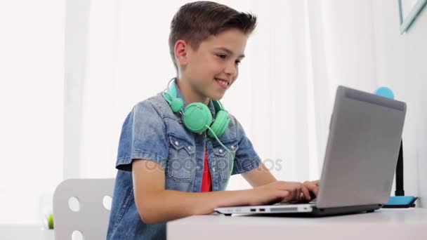 happy boy with headphones typing on laptop at home - Záběry, video