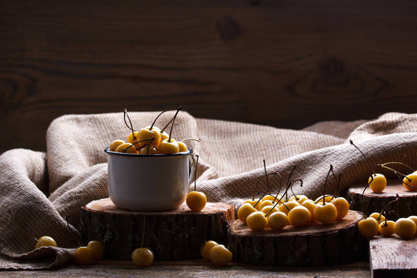 Yellow cherry in a rustic style on a wooden background. Berries of ripe fresh cherries in a cup. - Photo, Image
