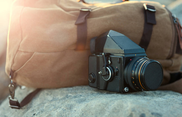 The film medium format camera is on the rocks next to the backpa - Foto, Imagem