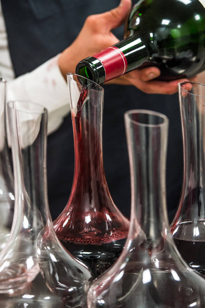 Sommelier at work, pouring wine to decanter while standing near the wine shelf - Photo, Image