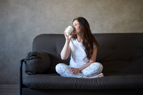 ソファでお茶を飲みながら座っている女性 - 写真・画像