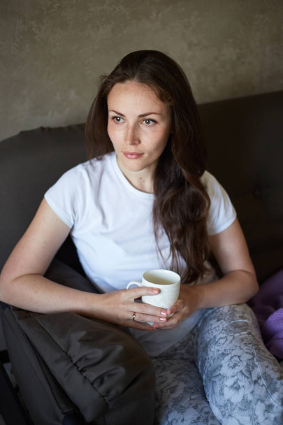 Woman sits on couch and drinking tea - Foto, imagen