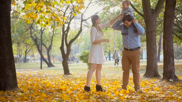 Roztomilý chlapeček sedí na ramenou otcové a těší mají čas s rodinou v parku - Záběry, video