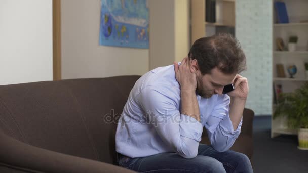 Sad man sitting on sofa and talking with boss on smartphone, problems and crisis - Кадри, відео