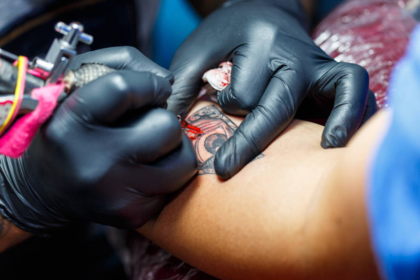 Primo piano tatuatore dimostra il processo di ottenere tatuaggio nero con vernice. Master lavora in guanti sterili neri
. - Foto, immagini
