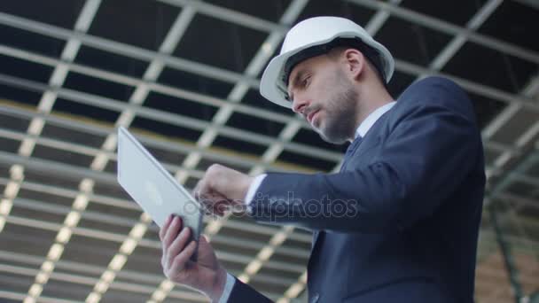Businessman in Hard Hat Walking, Talking, and Using Tablet Computer. Glass Building or Skyscraper under Construction on Background. - Materiał filmowy, wideo