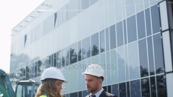 Female Engineer and Businessman in Hard Hats Having Conversation and using Tablet on Construction Site. Glass Building on Background. - Imágenes, Vídeo