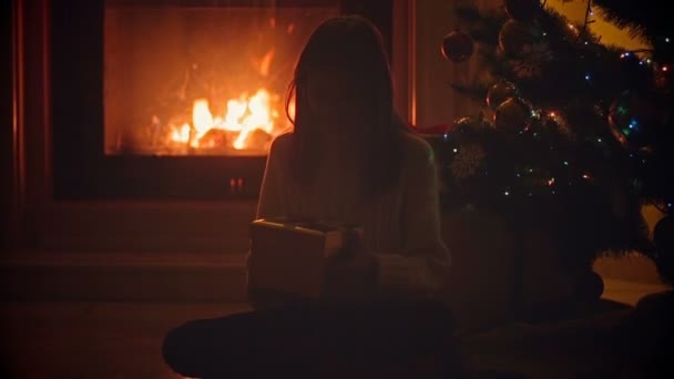 Portret van vrolijk meisje zitten bij de open haard in huis en op zoek binnenkant Christmas box met heden - Video
