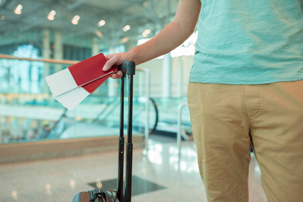 Крупный план паспортов с посадочным талоном и багажом в руках мужчин в аэропорту. Турист путешествует и ждет самолет
 - Фото, изображение