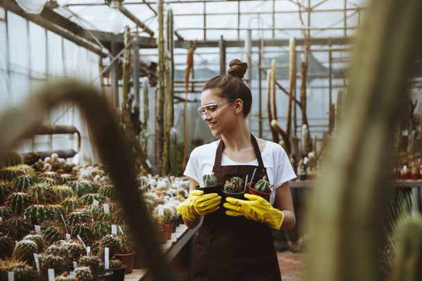 Happy young lady in glasses standing in greenhouse near plants. - Фото, изображение