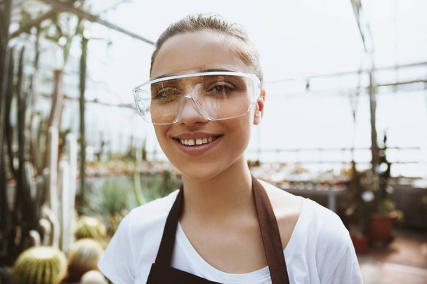 Pretty young woman in glasses standing in greenhouse - Фото, зображення