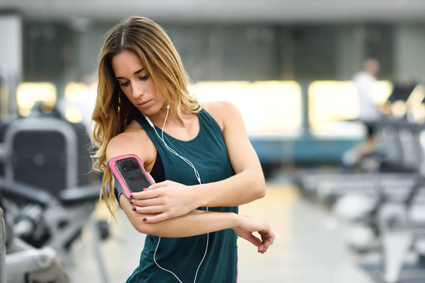 Jovem mulher usando smartphone em pé no ginásio
 - Foto, Imagem