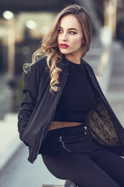 Beautiful young girl wearing black jacket sitting in the street. - Photo, Image