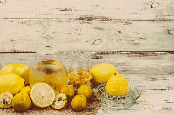 Fruit liquor in a glass bottle on rustic wooden table. Homemade alcohol made from fruit of lemon and quince - Fotoğraf, Görsel