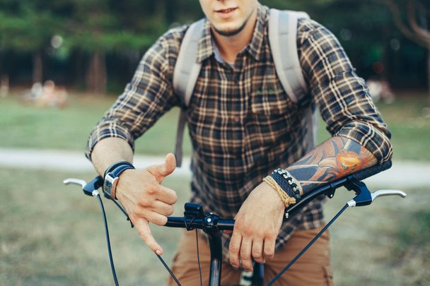 Młody człowiek pokazuje znak luźne (Shaka Surfer) zawiesić ręcznie, siedząc na rowerze na zielonej łące lato - Zdjęcie, obraz