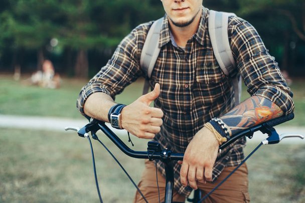 Young Man Is Making Thumb Up By Hands Sitting On A Bicycle On Green Summer Meadow - Foto, Bild