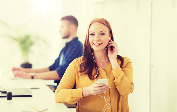 woman with earphones and smartphone at office - Foto, Bild