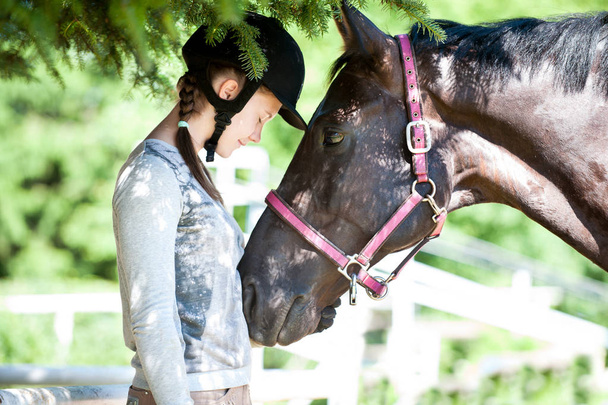 Νεαρή κοπέλα ιππασίας στέκεται κοντά σε καστανιές άλογο - Φωτογραφία, εικόνα