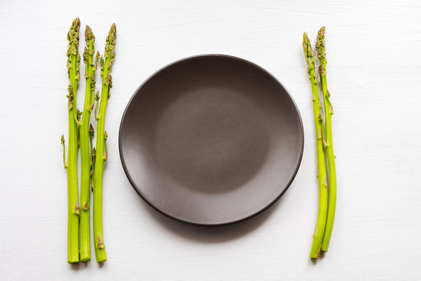 Fresh green asparagus and round empty brown bowl  - Фото, изображение