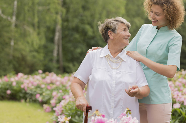 Enfermera y anciana con bastón en un jardín
 - Foto, imagen