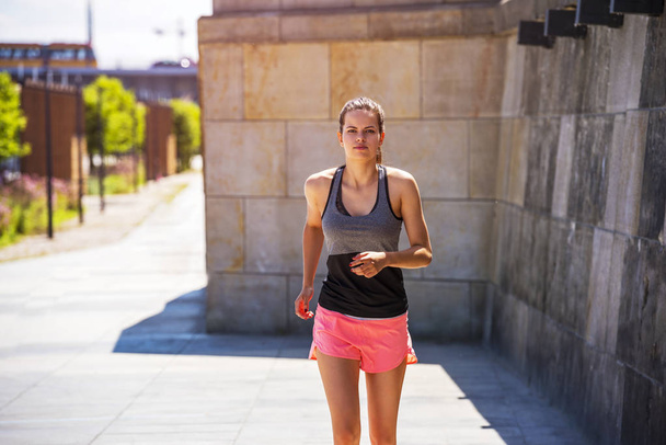 Urheileva nuori nainen juoksee jalkakäytävällä auringonvalossa. Terveyshaitat
 - Valokuva, kuva