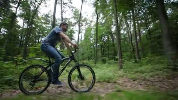 Steady cam view of man riding bycicle on forest road - Materiał filmowy, wideo