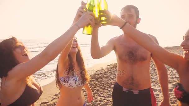 Zomertijd: Glimlachen vrienden Clinks bierflessen op het strand bij de zonsondergang - Video