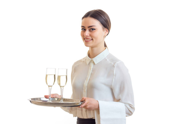 Очаровательная официантка в белой рубашке улыбается и держит два бокала вина на подносе, который
 - Фото, изображение