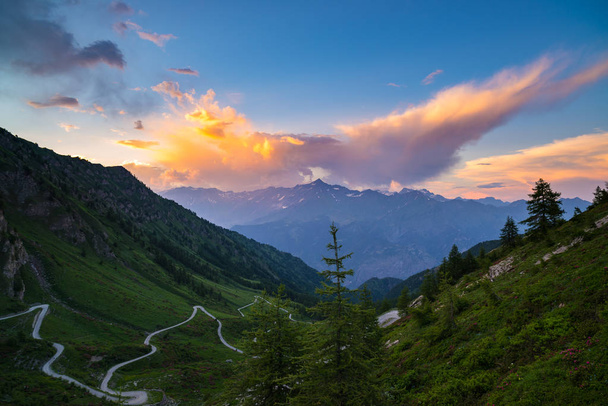 Dirt mountain road leading to high mountain pass in Italy (Colle delle Finestre). Expasive view at sunset, colorful dramatic sky, adventures in summer time, Italian Alps. - Photo, Image