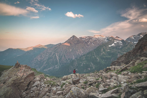 Una persona sentada en un terreno rocoso y observando un colorido amanecer en lo alto de los Alpes. Amplia vista angular desde arriba con brillantes picos de montaña en el fondo. Imagen tonificada
. - Foto, imagen