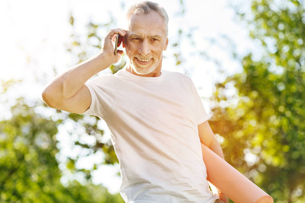Overjoyed aged man talking on phone in the park - Фото, зображення