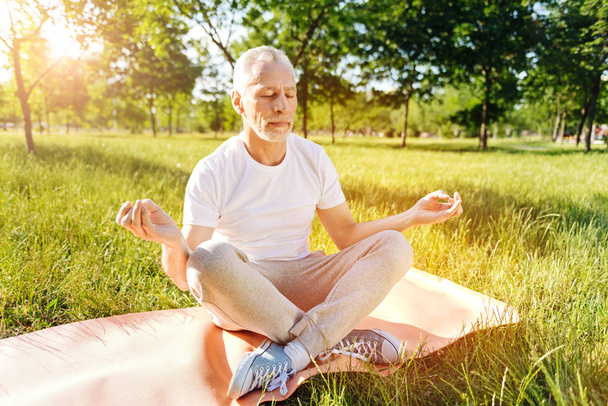 Peaceful aged man practicing yoga in the park - Фото, изображение