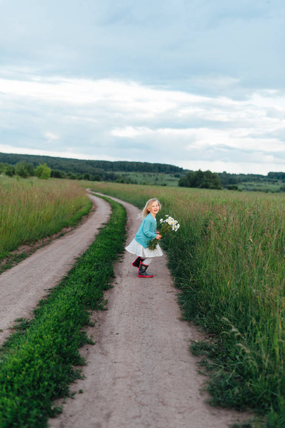 Un enfant joyeux court avec un bouquet de marguerites en bottes
 - Photo, image