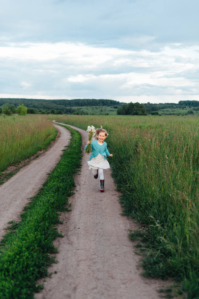Iloinen lapsi kulkee kukkakimpun kanssa saappaissa
 - Valokuva, kuva