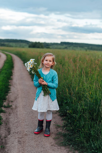 Enfant sur le chemin avec un bouquet de camomilles en bottes
 - Photo, image