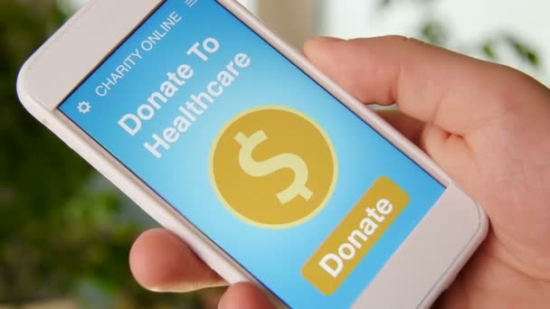 Man making an online donation to healtcare using charity applicaiton on smartphone - Footage, Video