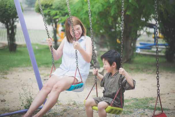 Азиатская мать и ее сын качаются на детской площадке
 - Фото, изображение