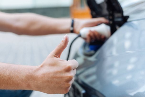 Male hand showing thumbs-up while charging an e-car - Foto, Bild
