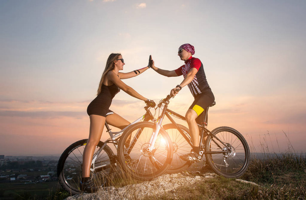 Cyclist couple with mountain bikes on the hill at sunset - Фото, изображение