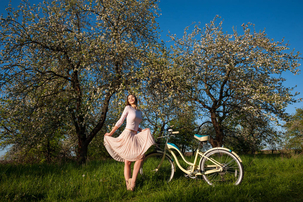 Hermosa ciclista femenina con bicicleta retro en el jardín de primavera
 - Foto, imagen