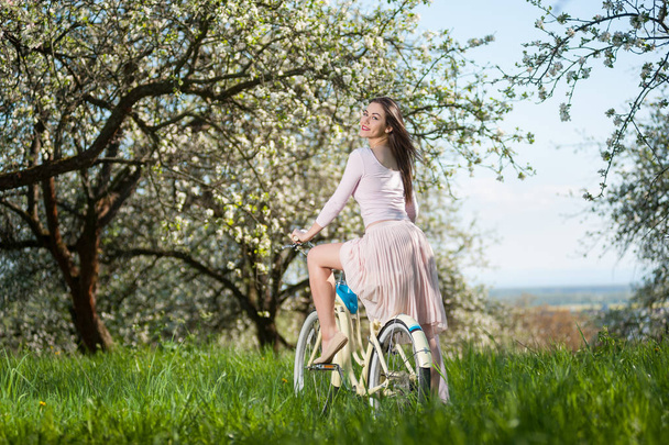 Hermosa ciclista femenina con bicicleta retro en el jardín de primavera
 - Foto, Imagen