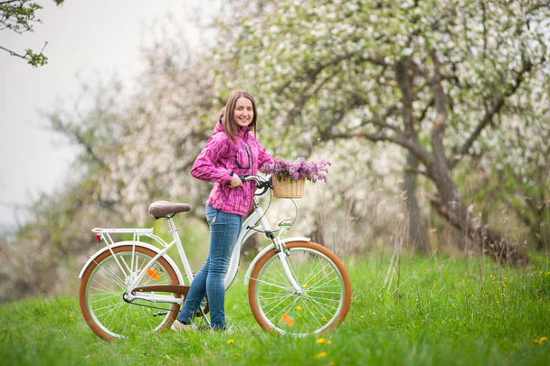 Жінка-велосипедистка з вінтажним білим велосипедом у весняному саду
 - Фото, зображення
