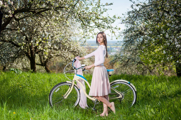 Beautiful female cyclist with retro bicycle in the spring garden - Photo, Image