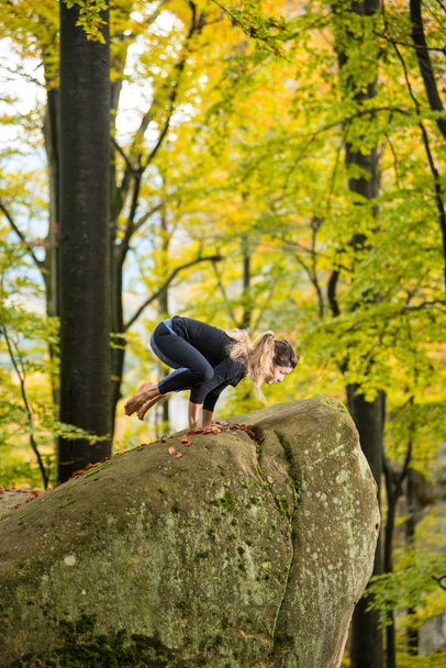 Mulher está praticando ioga na floresta de outono na grande pedra
 - Foto, Imagem