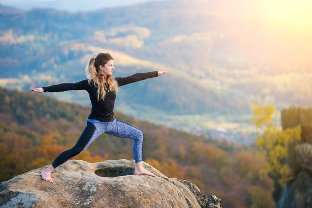 Sporty fit woman is practicing yoga on the top of the mountain - Photo, Image