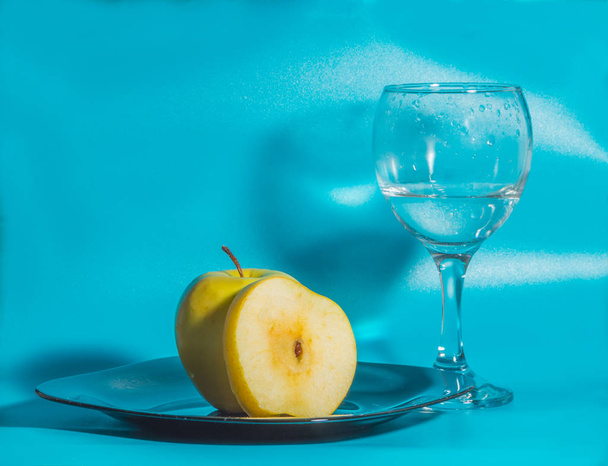 yellow Apple in the plate with a glass of water on a blue backgr - Фото, изображение