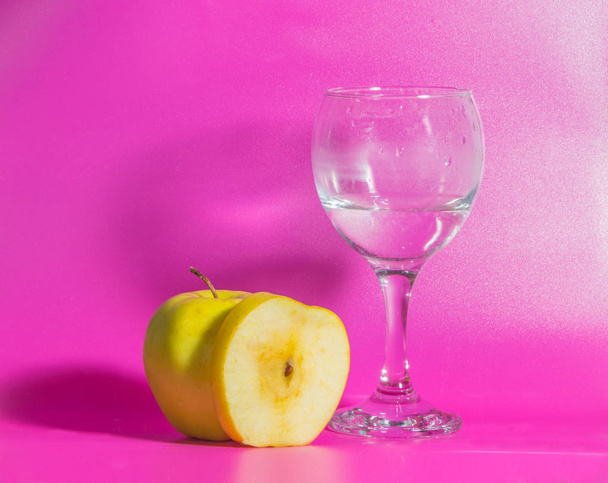 yellow Apple with a glass of water on a pink background. - Fotoğraf, Görsel